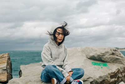 Man sitting on rock by sea against sky