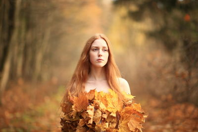 Portrait of beautiful young woman standing in forest during autumn