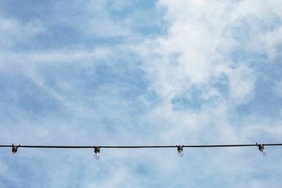 Low angle view of birds perching on cable against sky