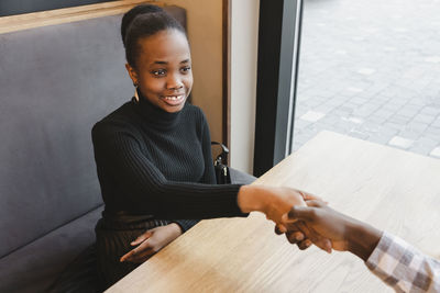 Happy young businesswoman shaking hand with businessman at cafe