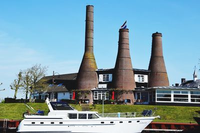 Boat moored by factory against blue sky