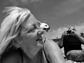 Man photographing woman with dog at beach against sky