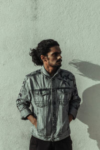 Young man looking away while standing against wall