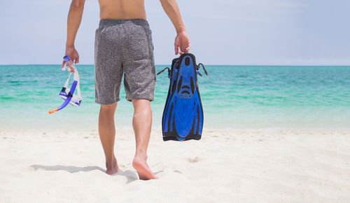 Low section of man walking with snorkel and diving flippers on beach