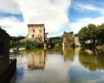 Old building by river against cloudy sky