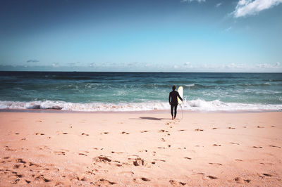 Full length of man with surfboard on beach against sky