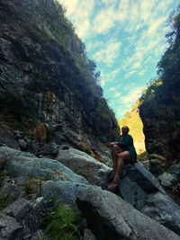 Rear view of man sitting on rock against sky