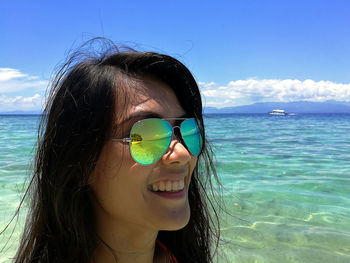 Portrait of young woman wearing sunglasses at beach against sky