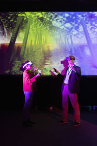 Multiracial colleagues with futuristic glasses gesturing by projection screen at workshop