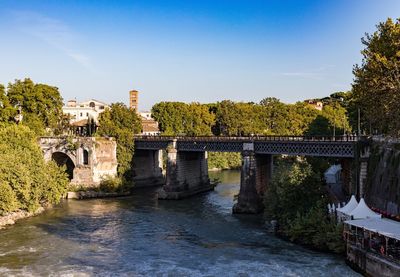Bridge over river by buildings against sky