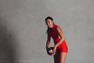 Portrait of smiling young woman standing against wall