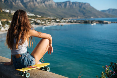 Woman sitting by sea against mountains