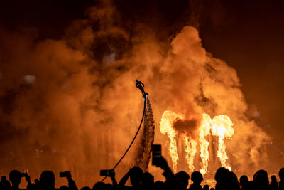 Group of people watching person flyboarding against firework display at night