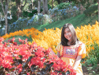 Portrait of smiling young woman standing amidst flowering plants