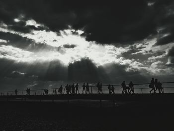 Silhouette people on calm sea against cloudy sky