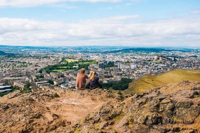 Rear view of couple sitting on mountain against residential district