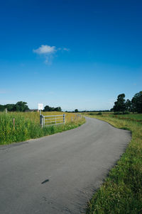 Empty road amidst grassy field against blue sky