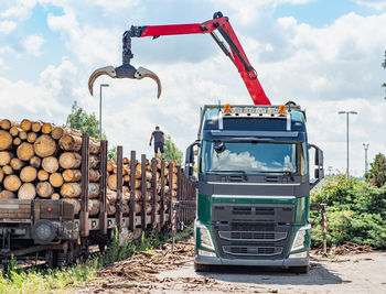 Road truck is loading the railway heavy wagon with spruce trunks. railway depot