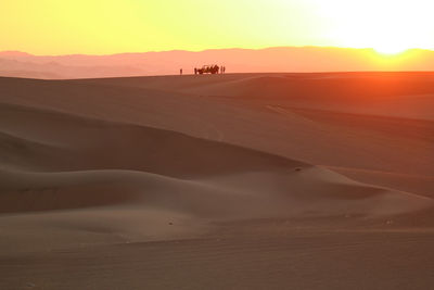 Sunset over sand dune of huacachina desert with the silhouette of dune baggy and people, ica, peru