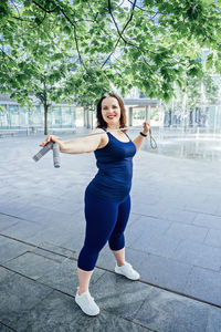 Confident plus size curvy happy young woman doing exercise workout with skipping rope outdoors.