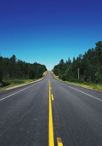 Road amidst trees against clear blue sky