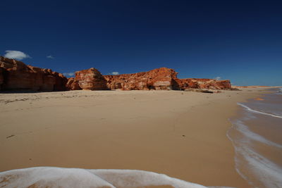 Rock formations on beach against clear blue sky