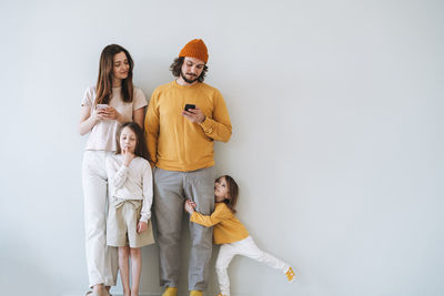 Young family with two children girls on gray wall background, parents using mobile phones