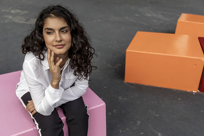 Portrait of young woman sitting against wall