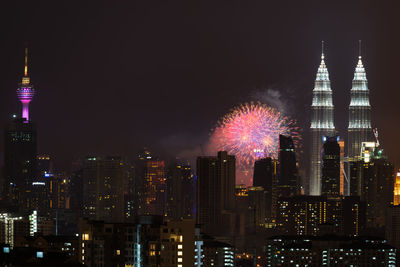 Firework display by illuminated petronas towers amidst buildings in city