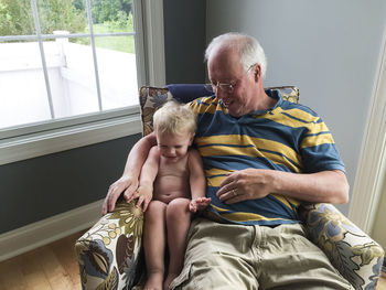 Blonde toddler boy laughs while sitting in chair with grandpa