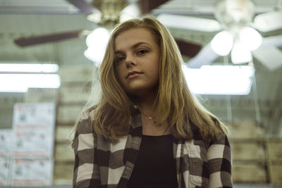 Low angle portrait of teenage girl standing against illuminated ceiling fans