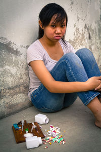 Depressed teenage girl sitting by narcotics against wall