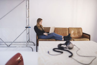 Full length side view of young woman using laptop while sitting on sofa at office