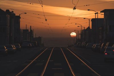 Railroad tracks amidst cars and buildings against sky during sunset