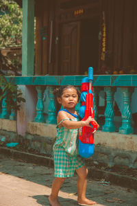 Portrait of cute girl with squirt gun walking on footpath
