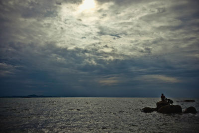 Man sitting on rock by sea against sky