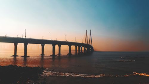 Bridge over sea against sky during sunset