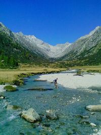 Man walking in river by mountains at parco naturale adamello brenta against clear blue sky