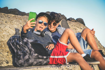 Brothers using mobile phone while sitting at beach