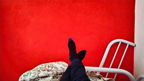 Low section of woman sitting against red wall