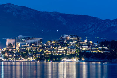 Illuminated city by sea against sky at night