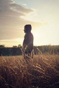 Side view of man standing on field against sky during sunset