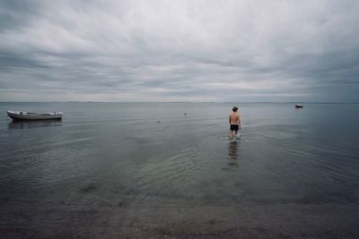 Rear view of shirtless man walking in sea against sky