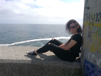 Young woman sitting on sea shore against sky