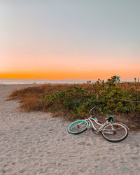 Bicycle on beach against sky during sunset