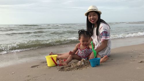 Smiling mother sitting with baby girl playing on shore at beach