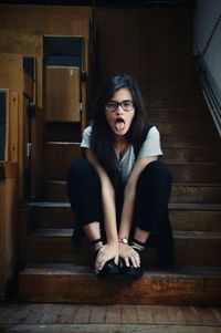 Young woman sticking out tongue while sitting on steps at home