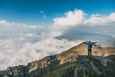 Woman standing on rock looking at mountain against sky