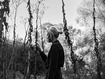 Side view of woman standing by plants in forest