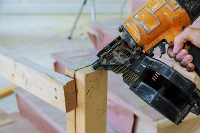 Close-up of hand holding nail gun by wood at workshop